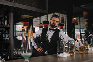 tired bartender leaning on bar counter and looking at dirty glasses and trash