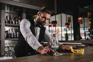 handsome bartender cleaning bar counter with rag