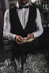 cropped image of bartender counting tips at bar counter
