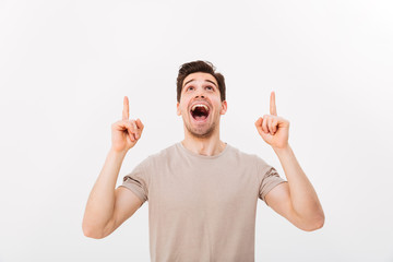 Young man in casual t-shirt looking upwards with pointing fingers on copyspace text or product,...