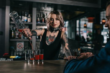 tattooed bartender making shot drinks for visitor at bar - obrazy, fototapety, plakaty