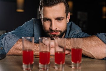 handsome visitor sitting at bar counter and looking at four shot drinks