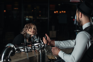 Plakat bartender pouring beer from beer taps into glass and looking at female visitor