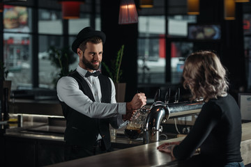 smiling bartender pouring beer from beer taps into glass and looking at visitor