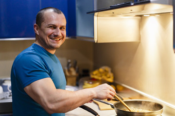 The man in the kitchen is cooking at home at the wok
