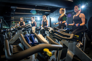 Group of young sporty women working out with dumbbells on cycling class at gym.