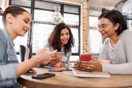 Advanced technology. Jolly merry three friends laughing while chatting and visiting cafe
