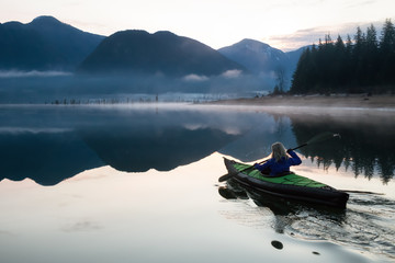 Adventurous Girl kayaking in a beautiful lake during a vibrant sunrise. Taken in Stave Lake, East of Vancouver, BC, Canada.