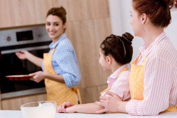 three generations of beautiful women in aprons baking pastry together at kitchen