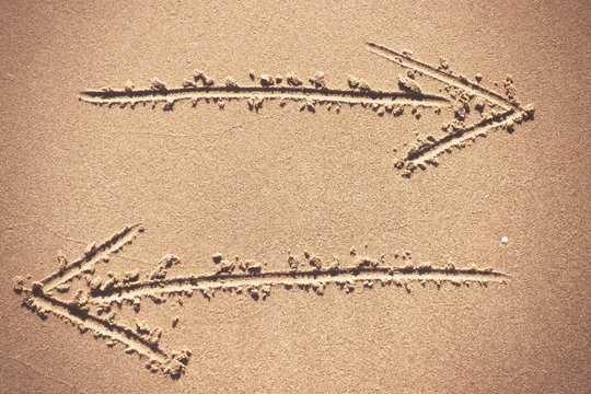 Two arrow signs drawing in sand background