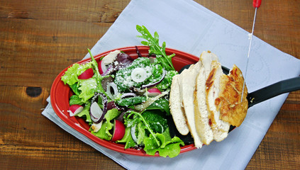 Juicy seared chicken breast slices are added to green tossed salad,  leaf vegetables, arugula, lettuce,baby  spinach on serving plate