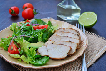 Juicy seared chicken breast sliced with nutritious green leaf vegetables, arugula, lettuce, spinach, cherry tomatoes and avocado.