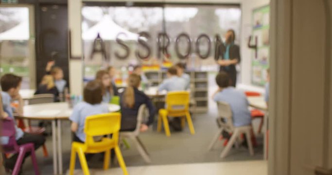 4K Elementary school children listening attentively to their teacher in classroom, seen through glass panel of the door. Slow motion