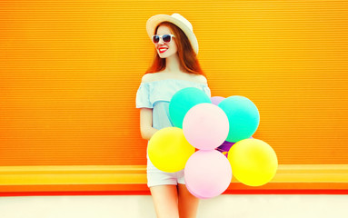 Fashion young woman with an air colorful balloons on a orange background