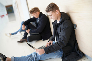Students in corridor websurfing with laptop