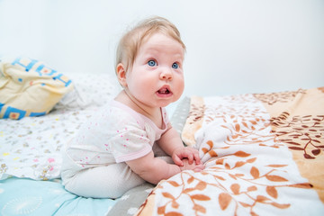 Funny baby girl sitting on the bed.