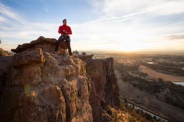 Adventurous man is rappeling down a cliff during a bright and vibrant sunny sunset. Taken in Smith Rock, Oregon, North America.