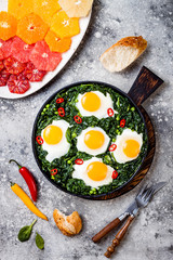 Green shakshuka with spinach, kale and peas. Healthy delicious breakfast with eggs, citrus salad. Top view, overhead, flat lay