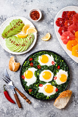 Naklejka na ściany i meble Green shakshuka with spinach, kale and peas. Healthy delicious breakfast with eggs, citrus salad, avocado. Top view, overhead, flat lay
