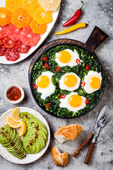 Green shakshuka with spinach, kale and peas. Healthy delicious breakfast with eggs, citrus salad, avocado. Top view, overhead, flat lay