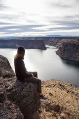 Fototapeta na wymiar Man is sitting at the edge of a cliff and enjoying the beautiful landscape. Taken at The Cove Palisades State Park in Oregon, North America.