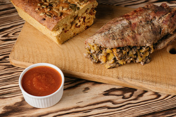 Pumpkin muffin and baked meat roll with filling along with a sauce on a wooden plate on a black background