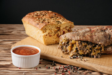 Pumpkin muffin and baked meat roll with filling along with a sauce on a wooden plate on a black background
