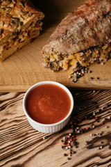 Pumpkin muffin and baked meat roll with filling along with a sauce on a wooden plate on a black background
