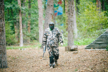 paintball player in protective uniform and mask aiming gun before shooting in summer.