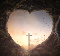Easter Religious concept: Heart shape of empty tomb stone with the cross over meadow sunrise background