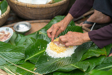 Making (wrapping) Chung Cake, the Vietnamese lunar new year Tet food outdoor with old woman hands and ingredients. Closed-up.