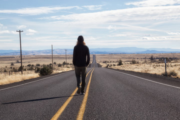 Man is standing in the middle of the long road during a vibrant sunny day. Taken in Oregon, North America.