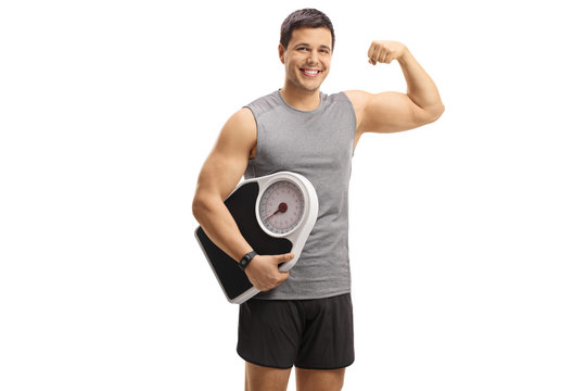 Young guy in sportswear holding a weight scale and flexing his biceps