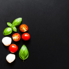 Fresh cherry tomatoes, basil leaf, mozzarella cheese on black slate stone chalkboard with copyspace. Healthy Italian traditional caprese salad ingredients. Organic Mediterranean food concept, flat lay