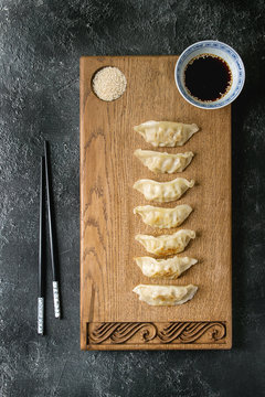 Asian dumplings Gyozas potstickers served with chopsticks and bowl of soy sesame sauce on asian style wooden board over black texture background. Top view, space.