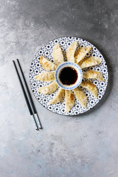 Asian dumplings Gyozas potstickers on white blue ceramic plate served with chopsticks and bowl of soy sesame sauce over grey texture background. Top view, copy space.