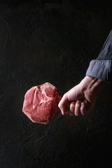 Man's hands holding raw uncooked black angus beef tomahawk steak on bone over dark background. Rustic style