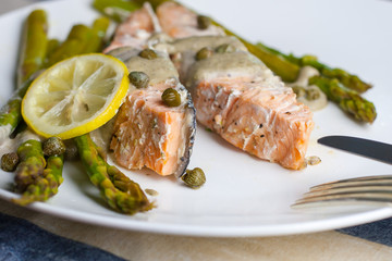 dish of cooked salmon with asparagus, lemon, capers and sauce on the plate