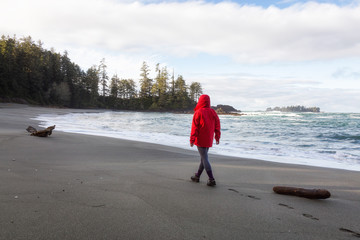Woman in a bright red jacket is enjoying the beautiful scenery of the sandy beach on Pacific Ocean Coast. Taken near Tofino, Vancouver Island, BC, Canada.