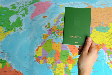 green  passport on the world map in women's hands