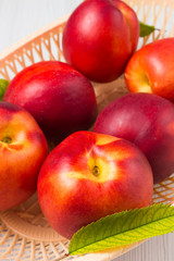 Peaches in a basket with leaves on a white wooden table in vertical composition
