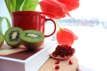 Morning concept. Red tulips and cup of coffee,  fresh pomegranate and kiwi on the book isolated. Close up