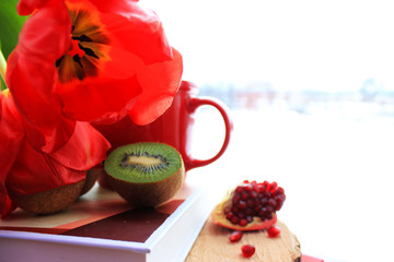 Morning concept. Red tulips and cup of coffee,  fresh pomegranate and kiwi on the book isolated. Close up