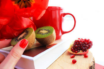 Morning concept. Red tulips and cup of coffee,  fresh pomegranate and kiwi on the book isolated. Close up