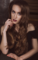 Portrait of an attractive brown-haired woman with a hair style in a Hollywood wave style, in a black dress with open shoulders. Studio photo. Fashion photo.