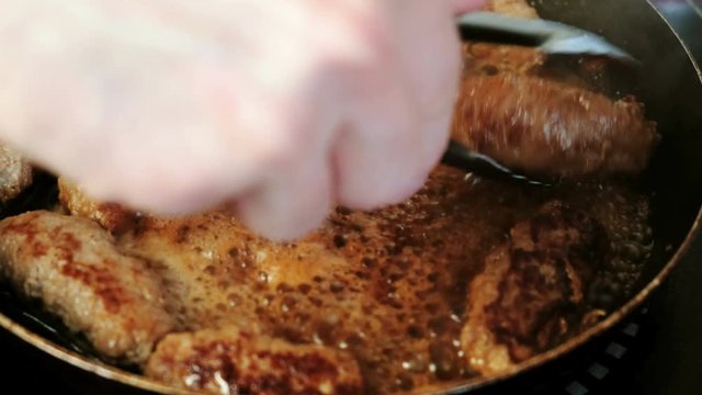 Men's hands with metal tongs turn around fried cutlets in a pan. Close-up view.