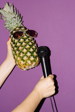 pineapple in earphones hand with microphone stretches to pineapple in earphones