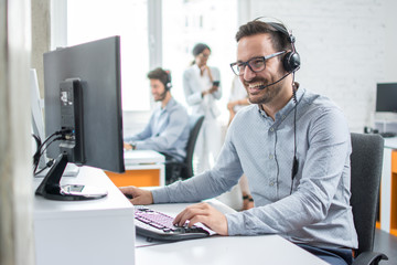 Smiling customer support operator with hands-free headset working in the office. - obrazy, fototapety, plakaty