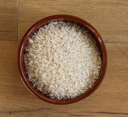 Stone bowl with uncooked white rice on wooden background