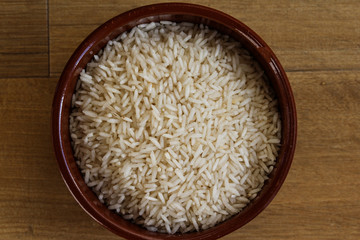 Stone bowl with uncooked white rice on wooden background